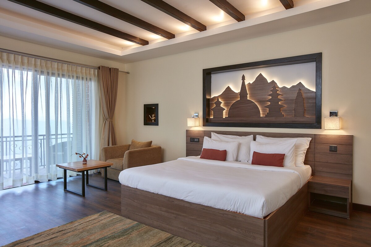 Habitación de hotel con una cama grande, zona de estar con una mesa y vistas al exterior.