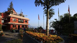 A red building with a balcony, surrounded by a garden with various plants and flowers.