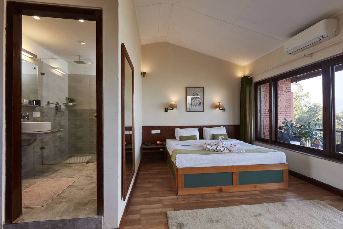A bedroom with a bed, bedside tables, a window with a view, and a bathroom with a shower and sink.