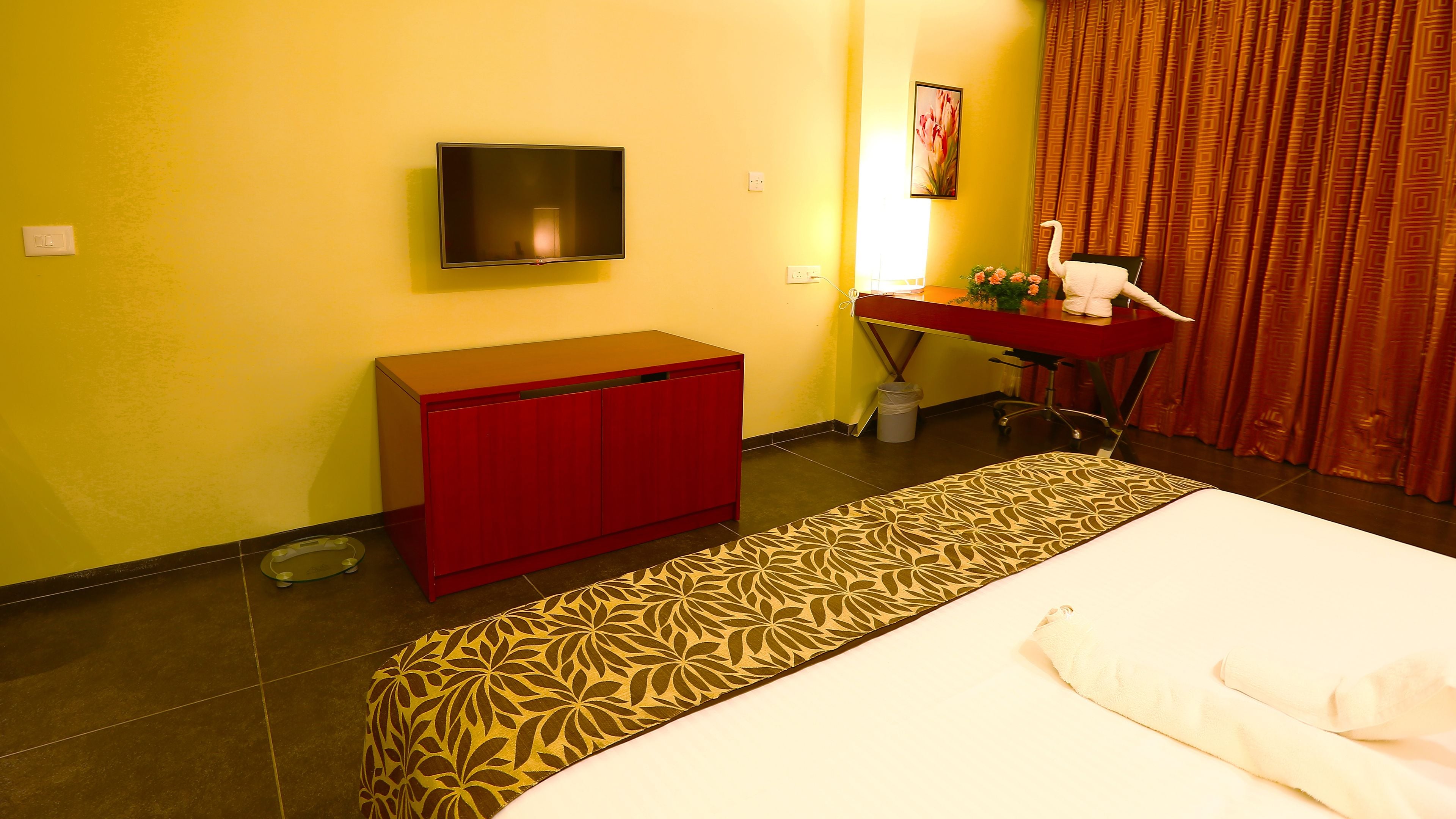 A hotel room with a bed, a red desk, a television, and a patterned rug.