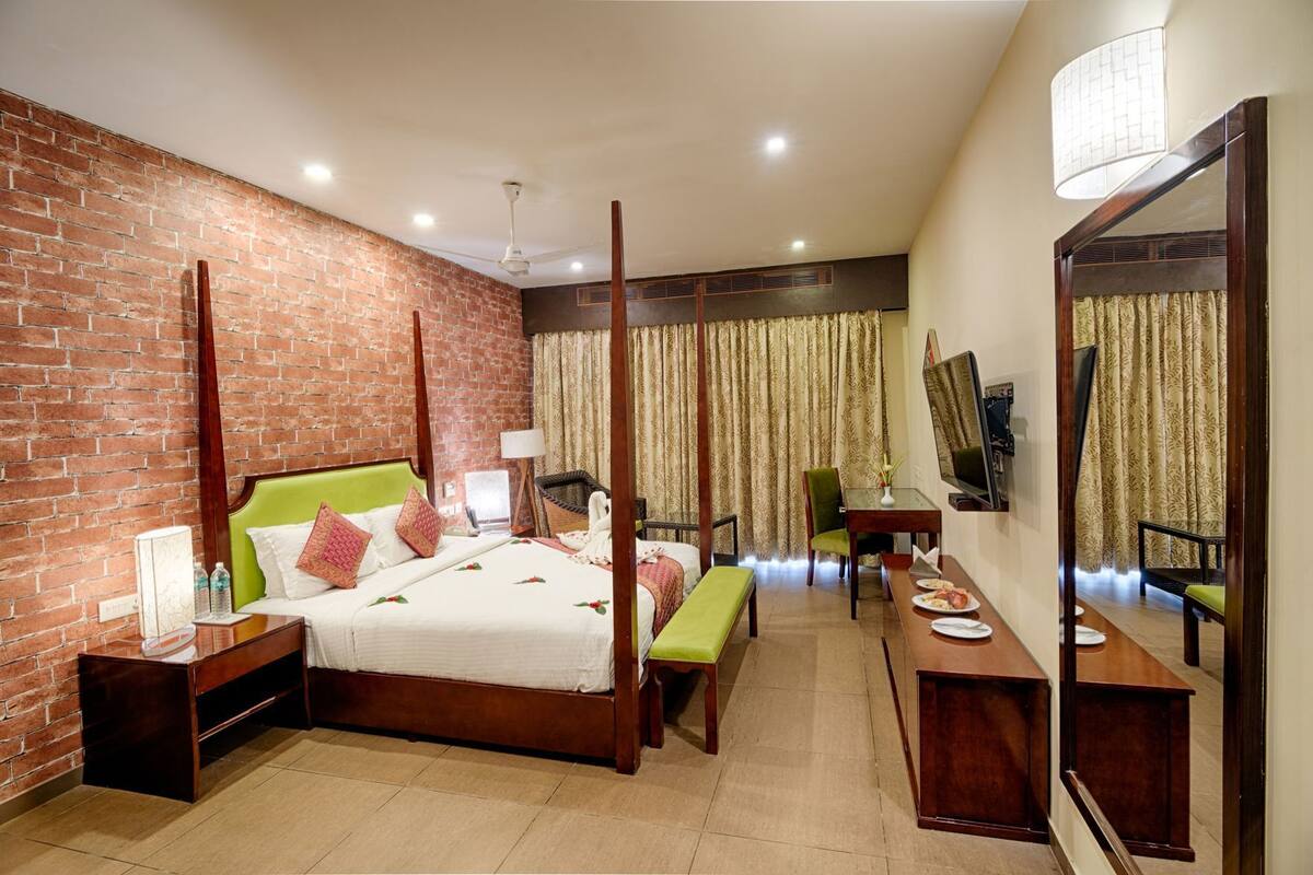 Quarto de hotel com parede de tijolos, cama de dossel, área de estar com mesa e cadeiras, e um espelho grande.
