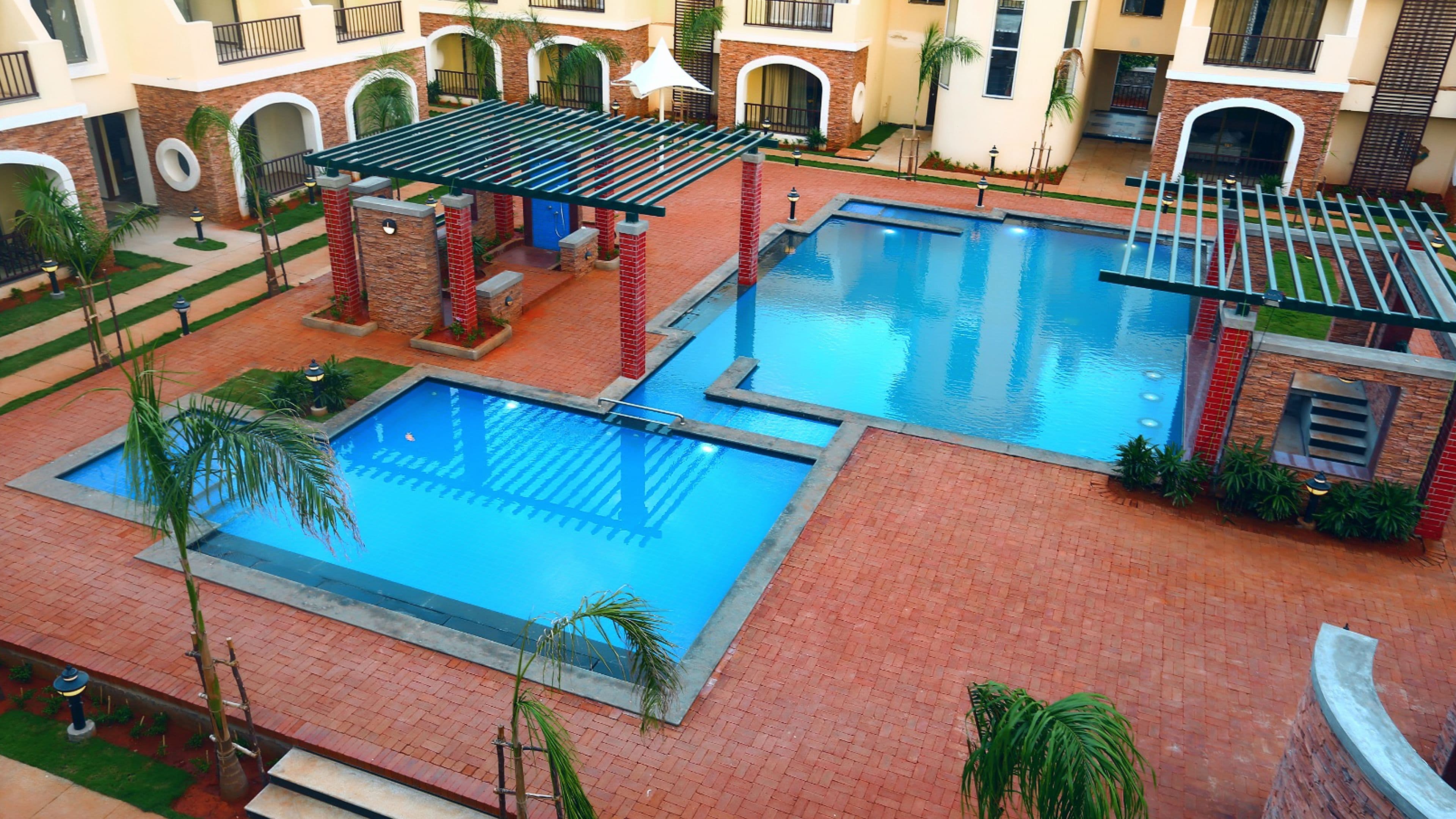 A pool area with two pools, a pergola, and a brick pathway.