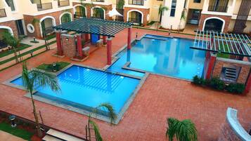 A pool area with two pools, a pergola, and a brick pathway.