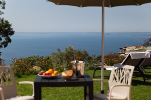 Una mesa con frutas, una bebida y un balde, al aire libre con vista al mar y las colinas.
