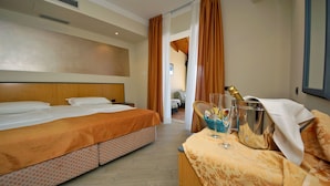 Habitación de hotel con una cama, una mesita de noche con una botella de champán, vasos y una cesta de fruta.