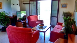 A living room with a television, red furniture, and a potted plant. - Windmill Complex (Sifnos)