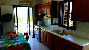 A kitchen with wooden cabinets, a microwave, a sink, and a dining area with a table and chairs. - Windmill Complex (Sifnos)