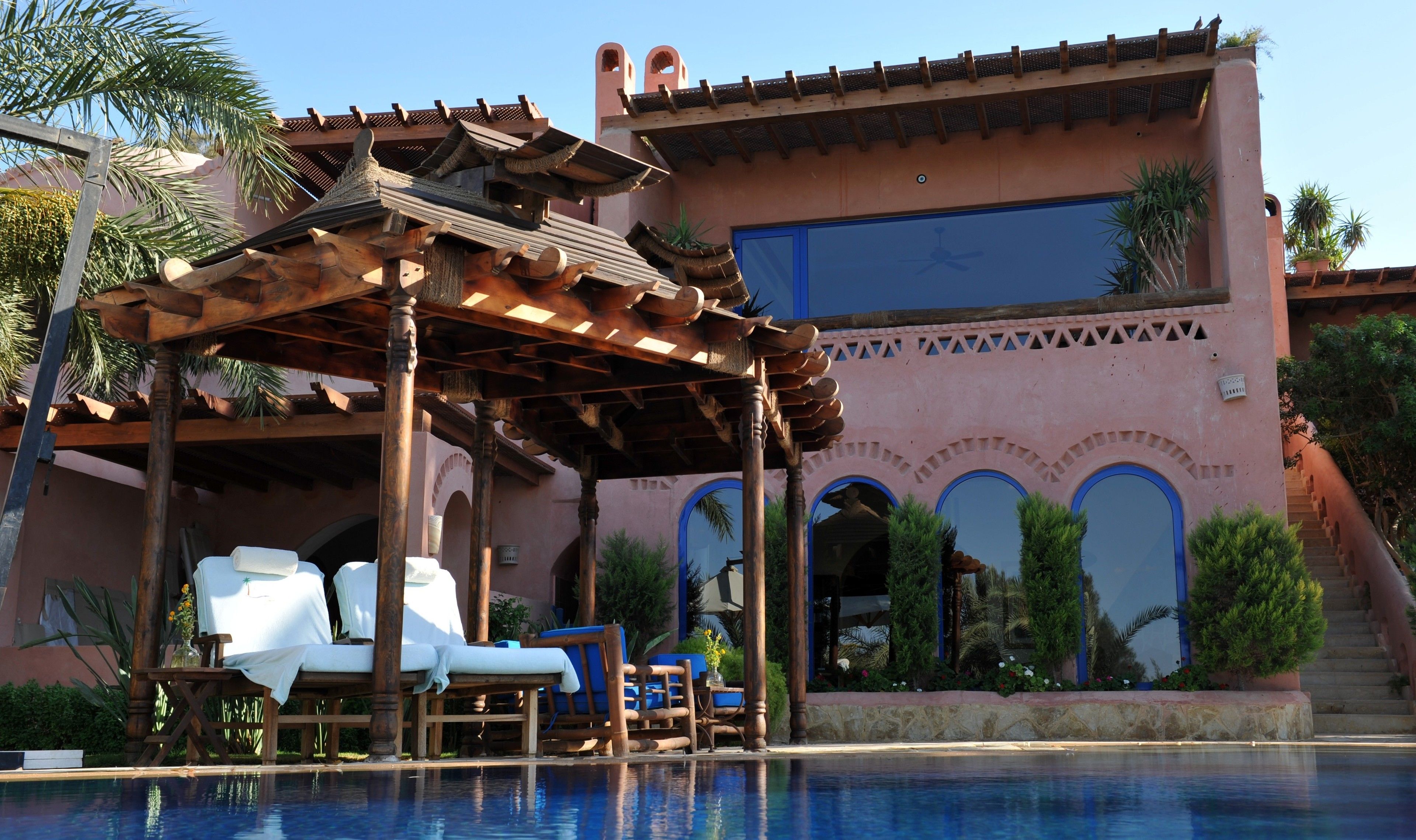 Un área de piscina con sillones de madera y un pérgola.
