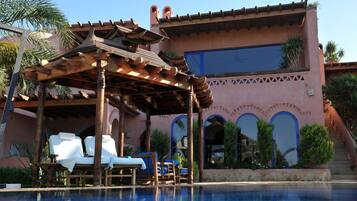 Un área de piscina con sillones de madera y un pérgola.