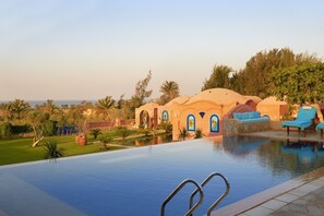 A pool area with a clear view of the pool, lounge chairs, and a building with arched windows. - Lazib Inn Resort & Spa (Yusuf as-Sidiq)