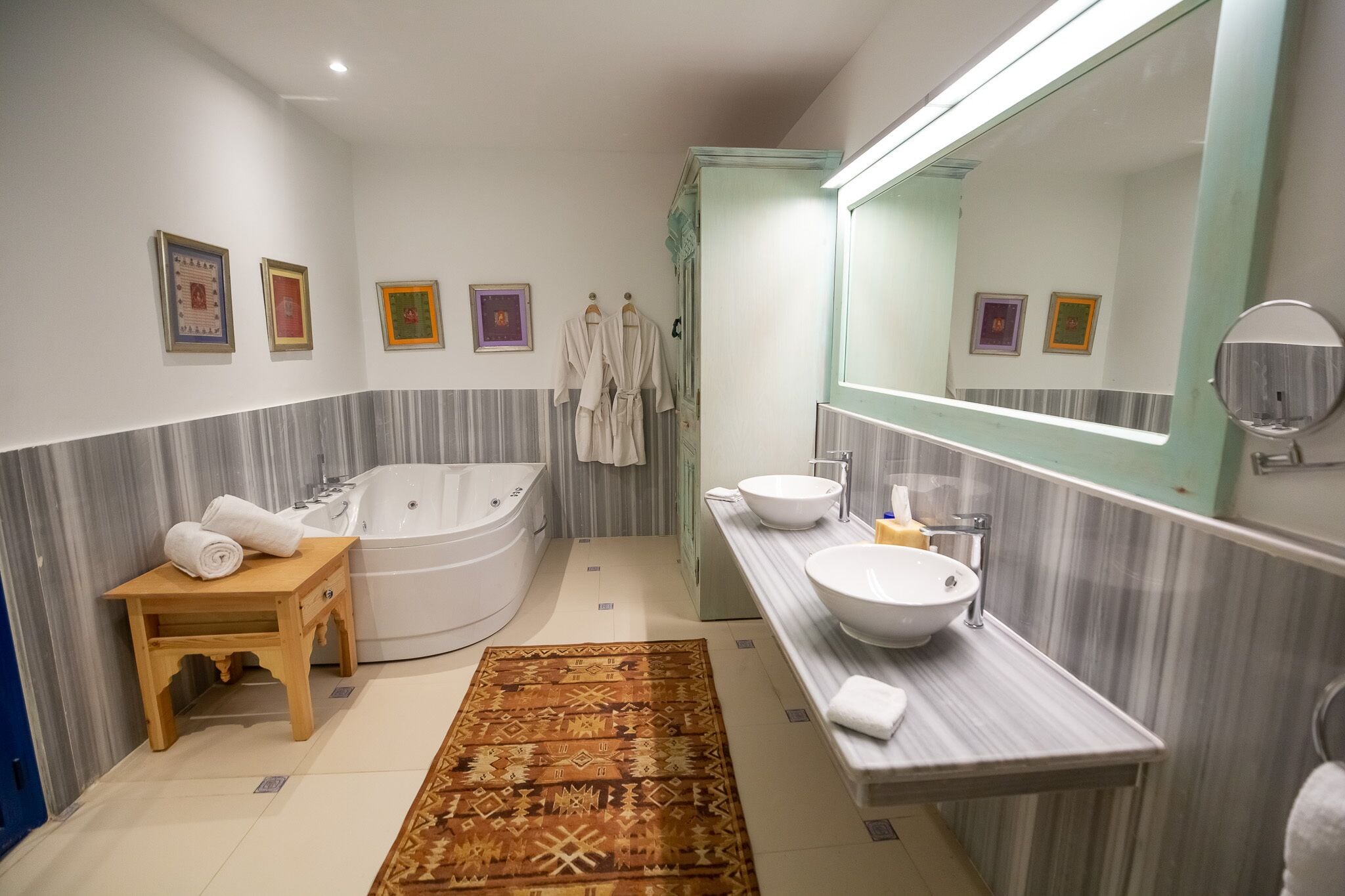 Une salle de bain moderne avec une baignoire, un grand miroir, un meuble-lavabo et un petit tabouret en bois sur lequel sont posées des serviettes.