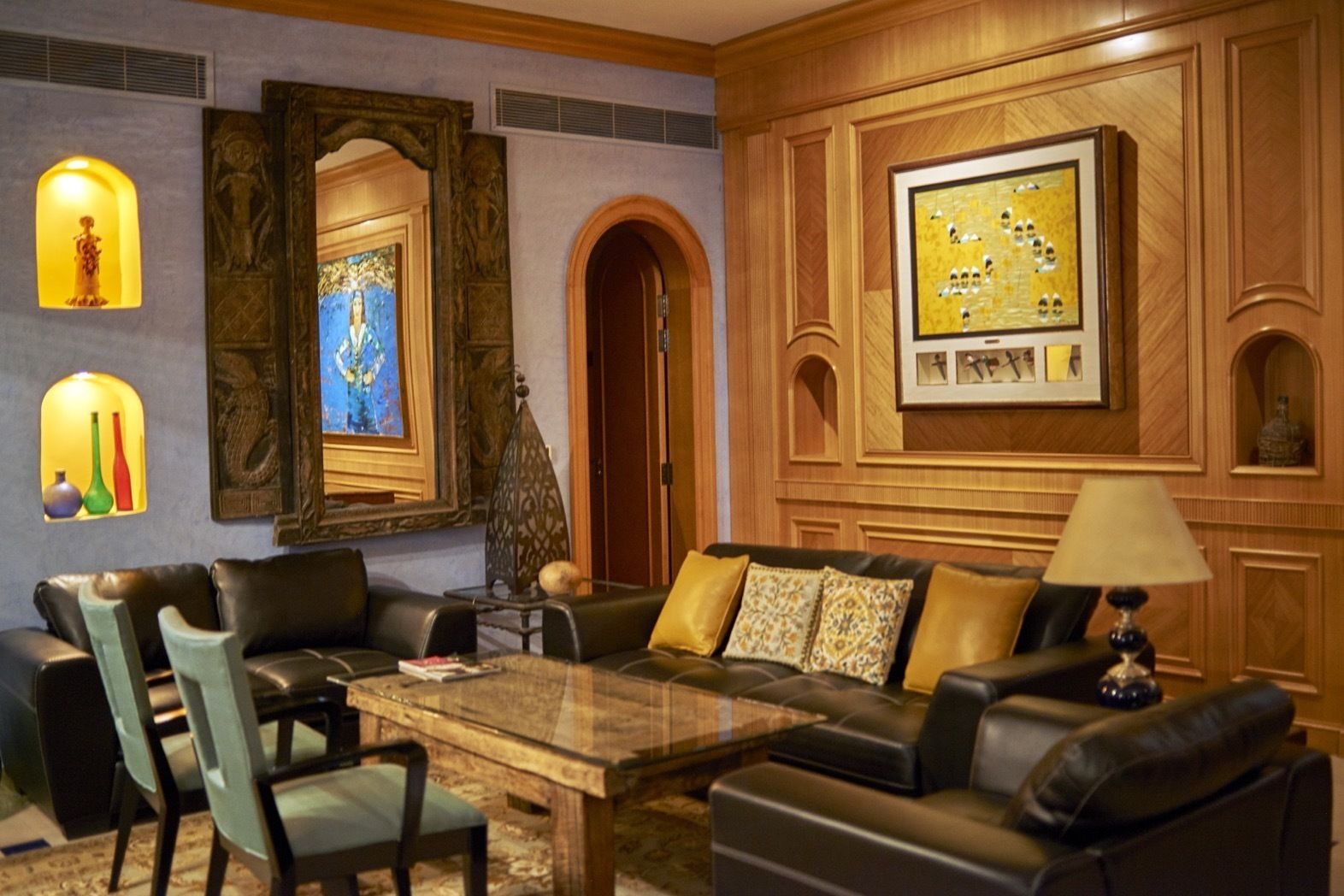 A modern living room with a leather sofa, a glass coffee table, and a wooden accent wall with framed artwork.