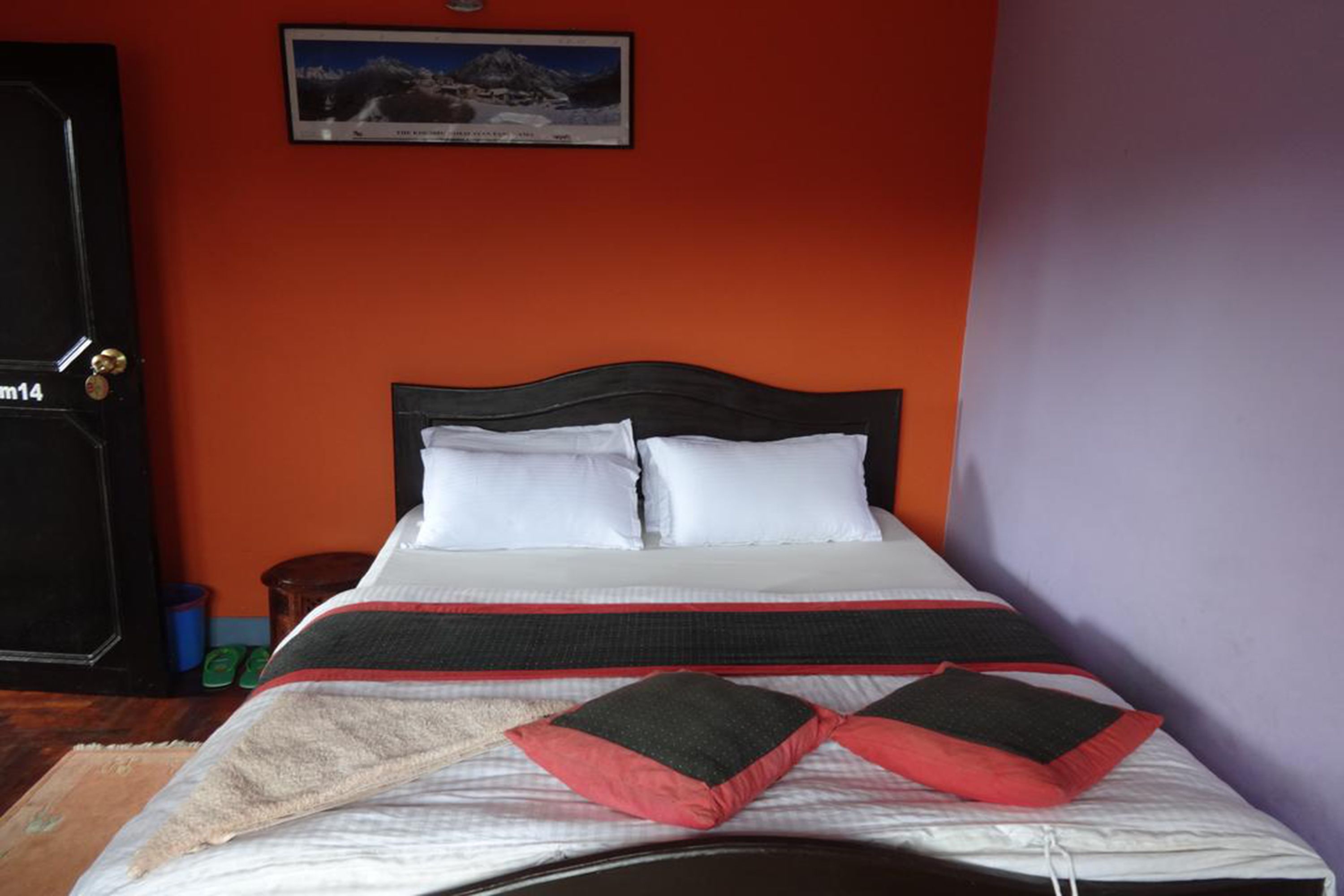 A neatly made bed with a black headboard, white pillows, and a red and black bedspread.