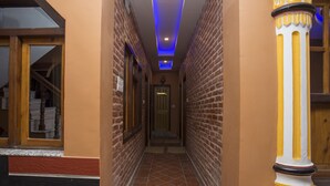 Un pasillo con paredes de ladrillo, piso de baldosas y una puerta de madera al final.