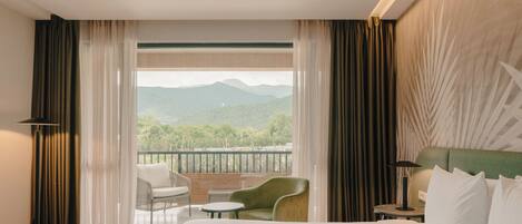 Une chambre d’hôtel avec un grand lit, un balcon offrant une vue sur les montagnes, une chaise, une petite table et une lampe.