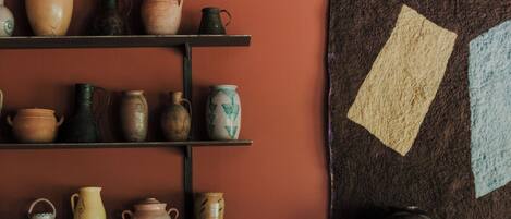 A room with a brick fireplace, shelves with pottery, and a wall with a geometric tapestry.