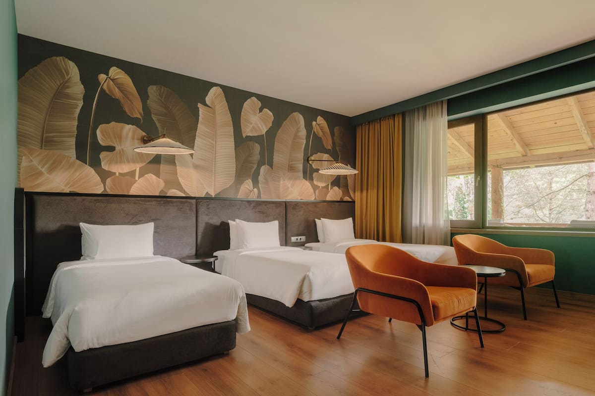 A hotel room with two beds, a seating area with orange chairs, and a large window with curtains.