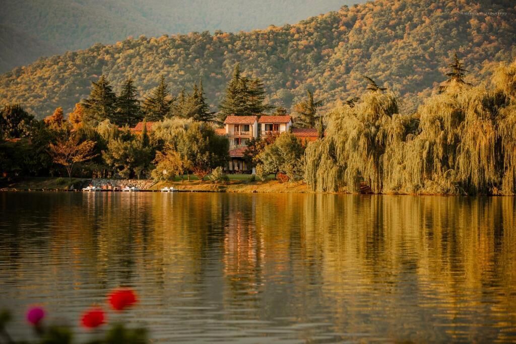 A house by a lake with a forested hillside in the background.