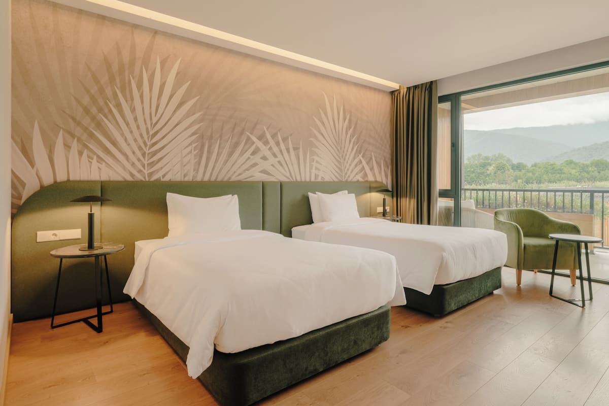 A hotel room with two beds, a view of the outdoors, and a balcony.