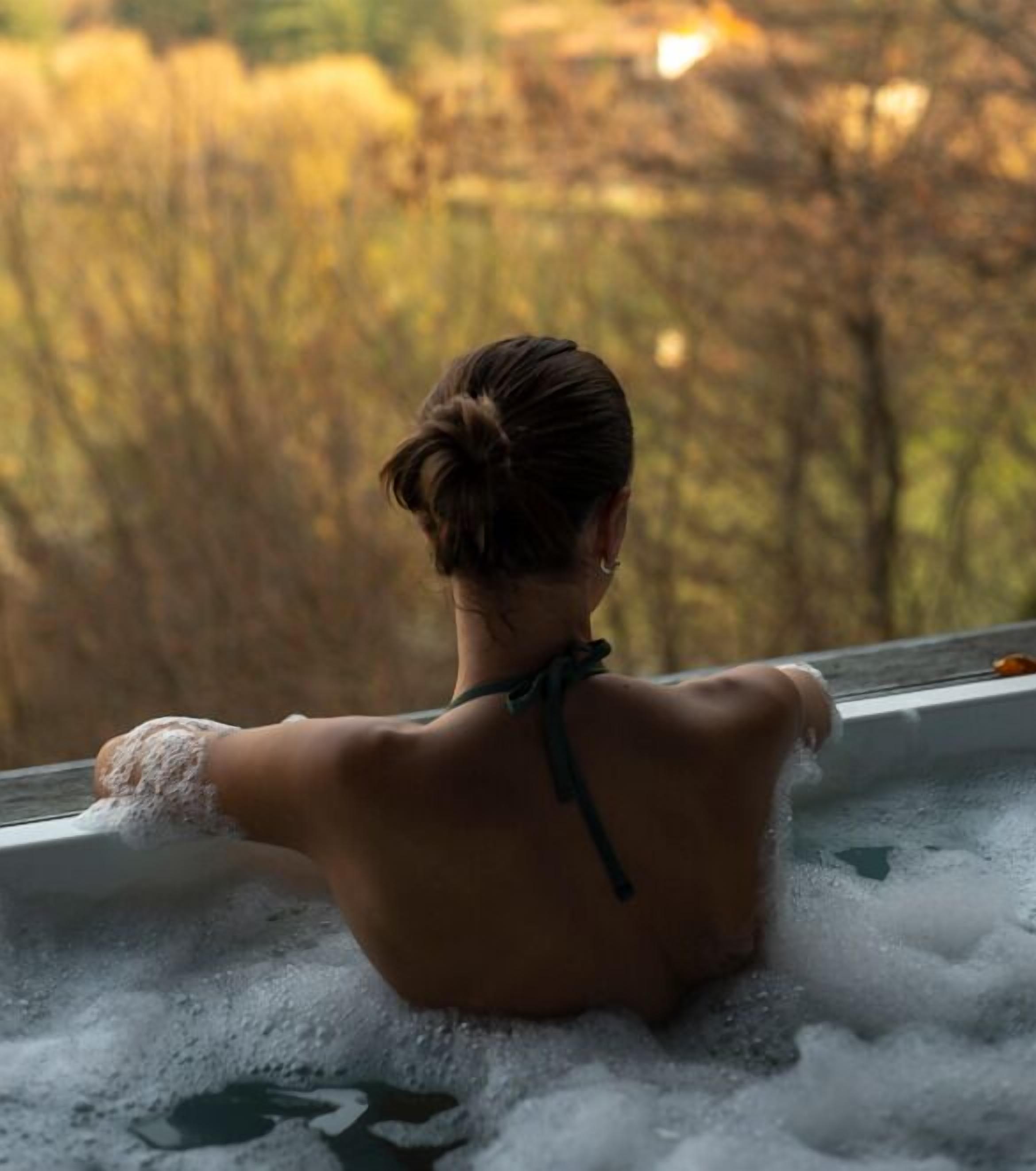 A person in a bathtub with a view of trees outside.