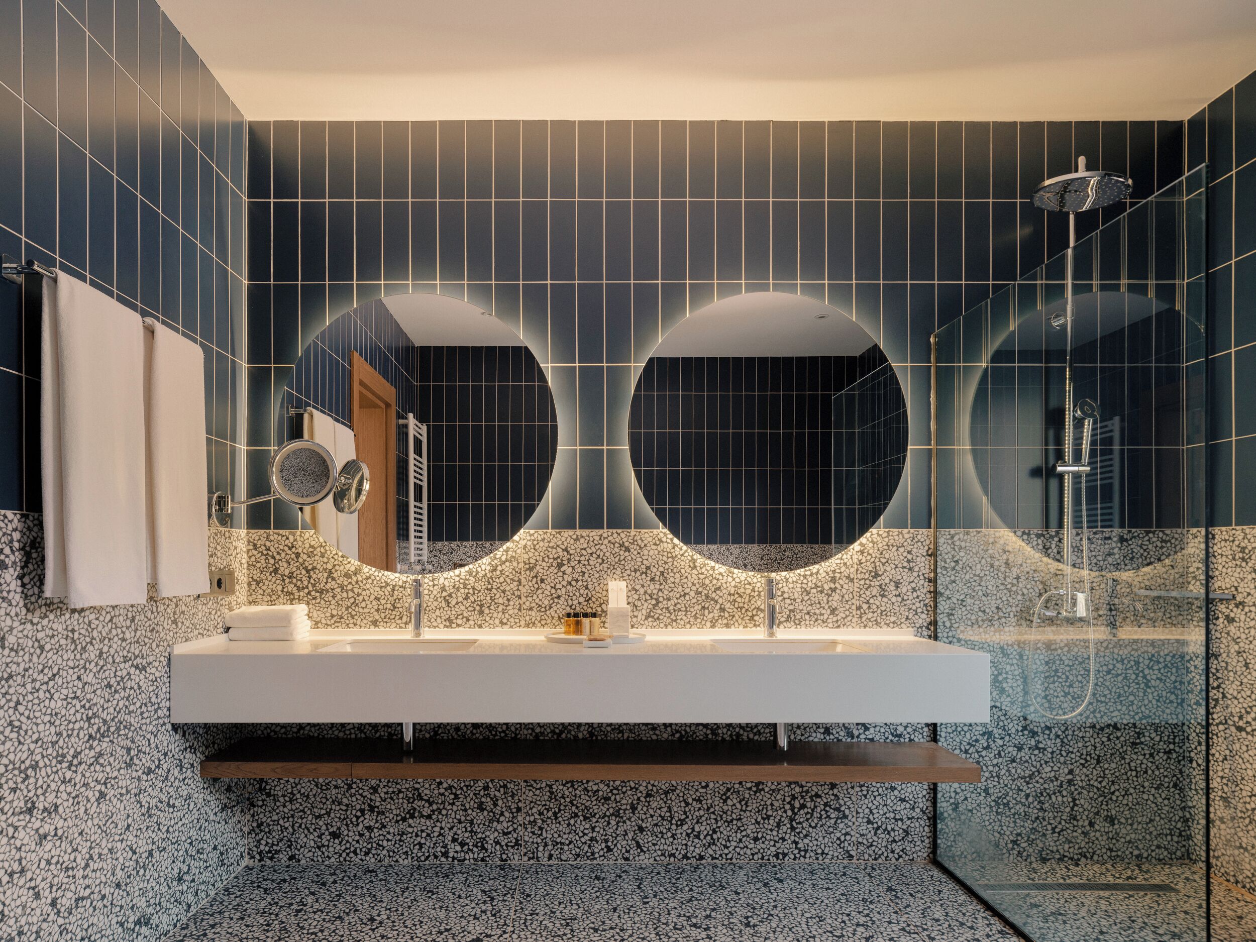 A modern bathroom with a large mirror, two circular mirrors, a white sink, and a shower area.