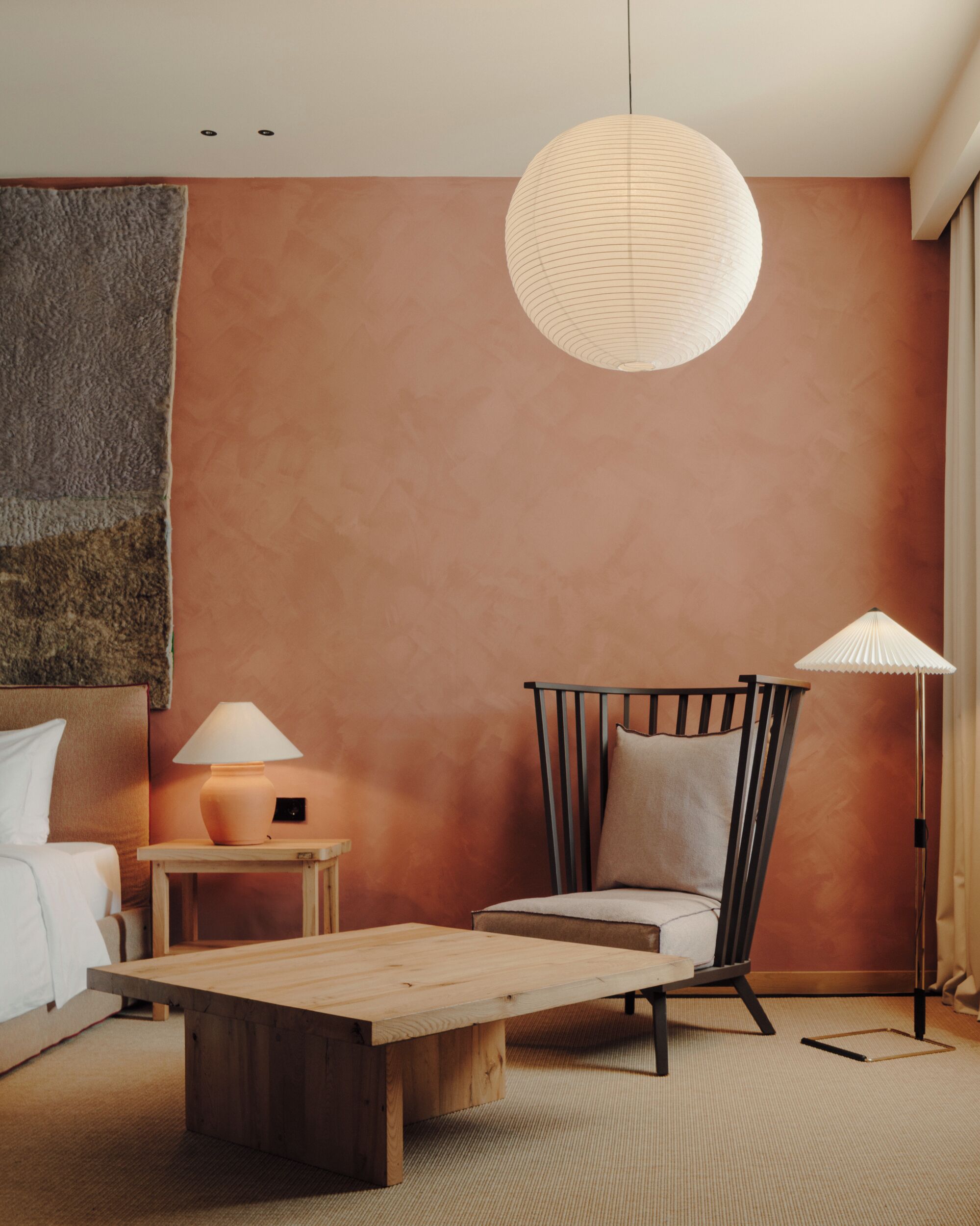 Una habitación de hotel moderna con una cama y una mesita de madera, una silla, una lámpara de pie y una lámpara de pared.