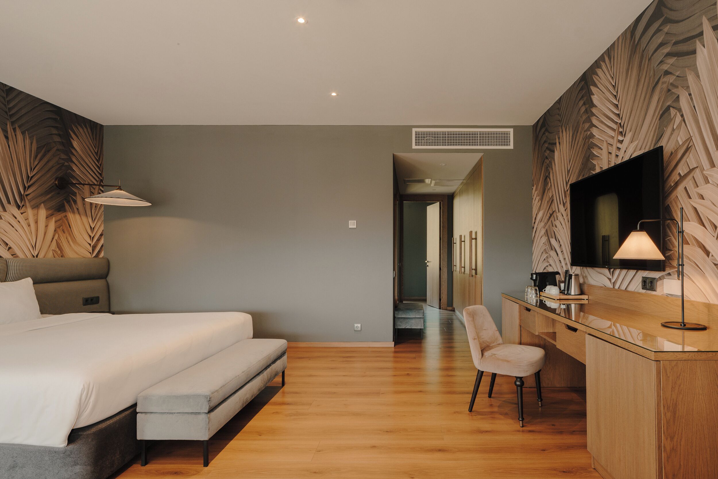 A modern hotel room with a large bed, a desk with a chair, a flat-screen TV, and a large window.