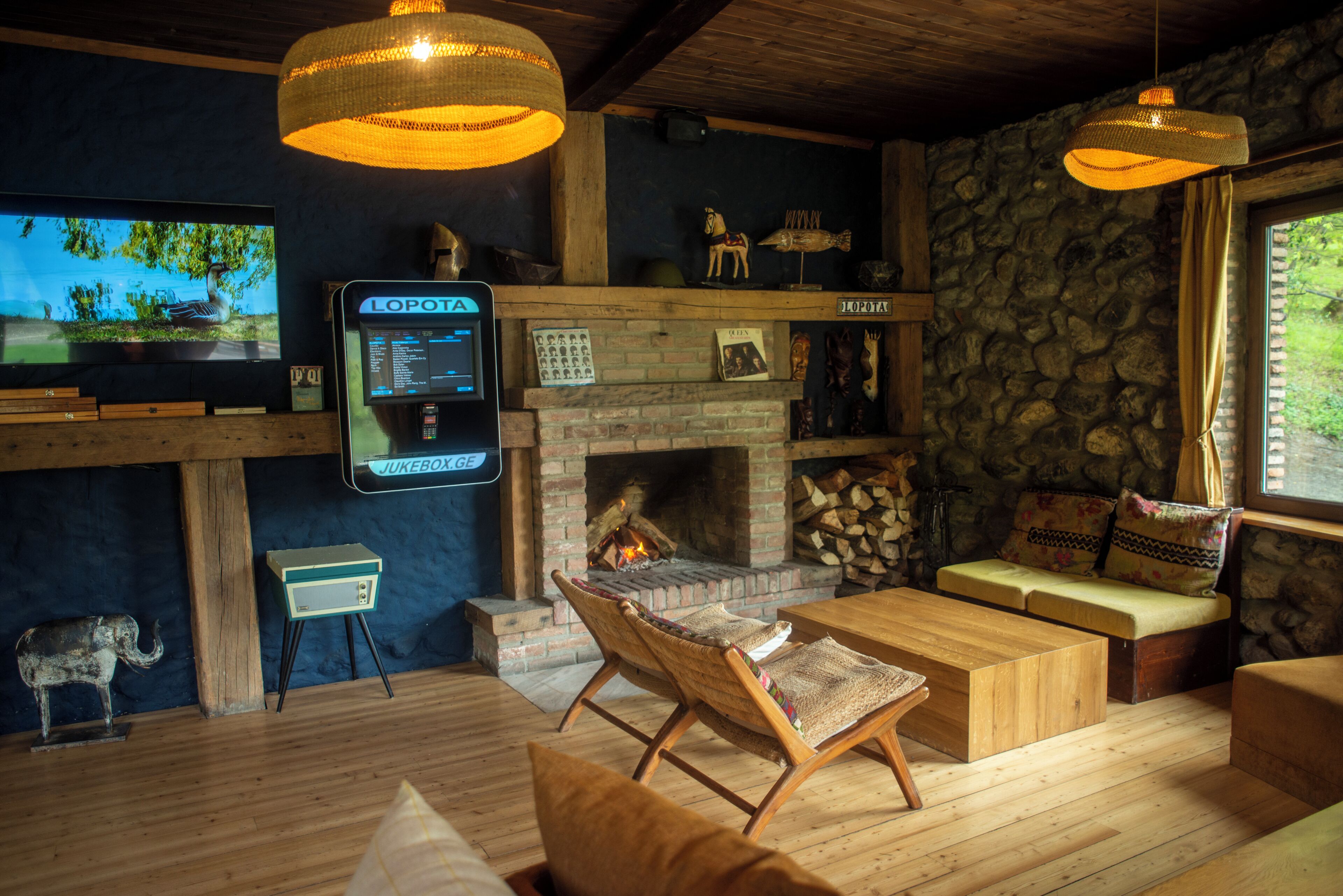 A cozy living room with a fireplace, wooden furniture, a television, and a jukebox.