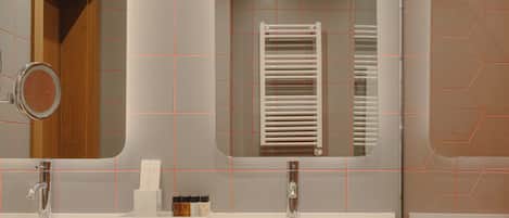 A modern bathroom with two sinks, a mirror, and a towel rack.
