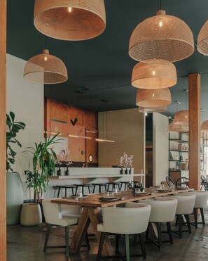 Un espace de restauration moderne avec des tables en bois, des chaises blanches et de grandes suspensions en fibres tressées.