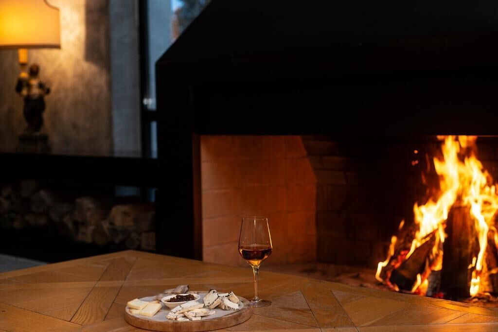 A table with a glass of wine and a plate of oysters in front of a fireplace.