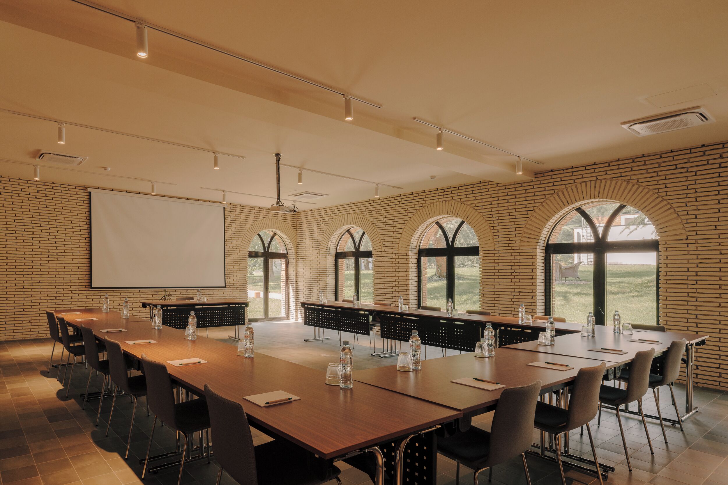 A conference room with a long table, chairs, a projector screen, and large windows.