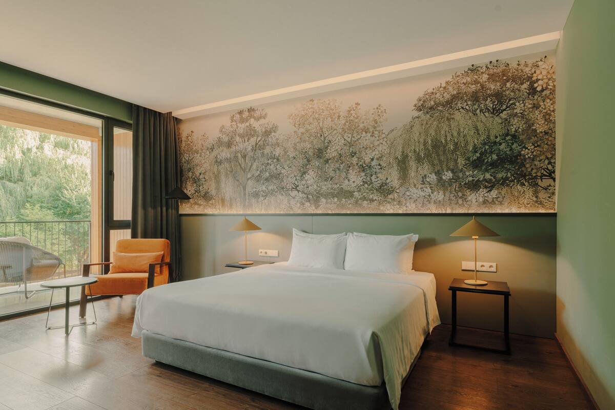A bedroom with a bed, two bedside tables, a chair, and a large wall mural.