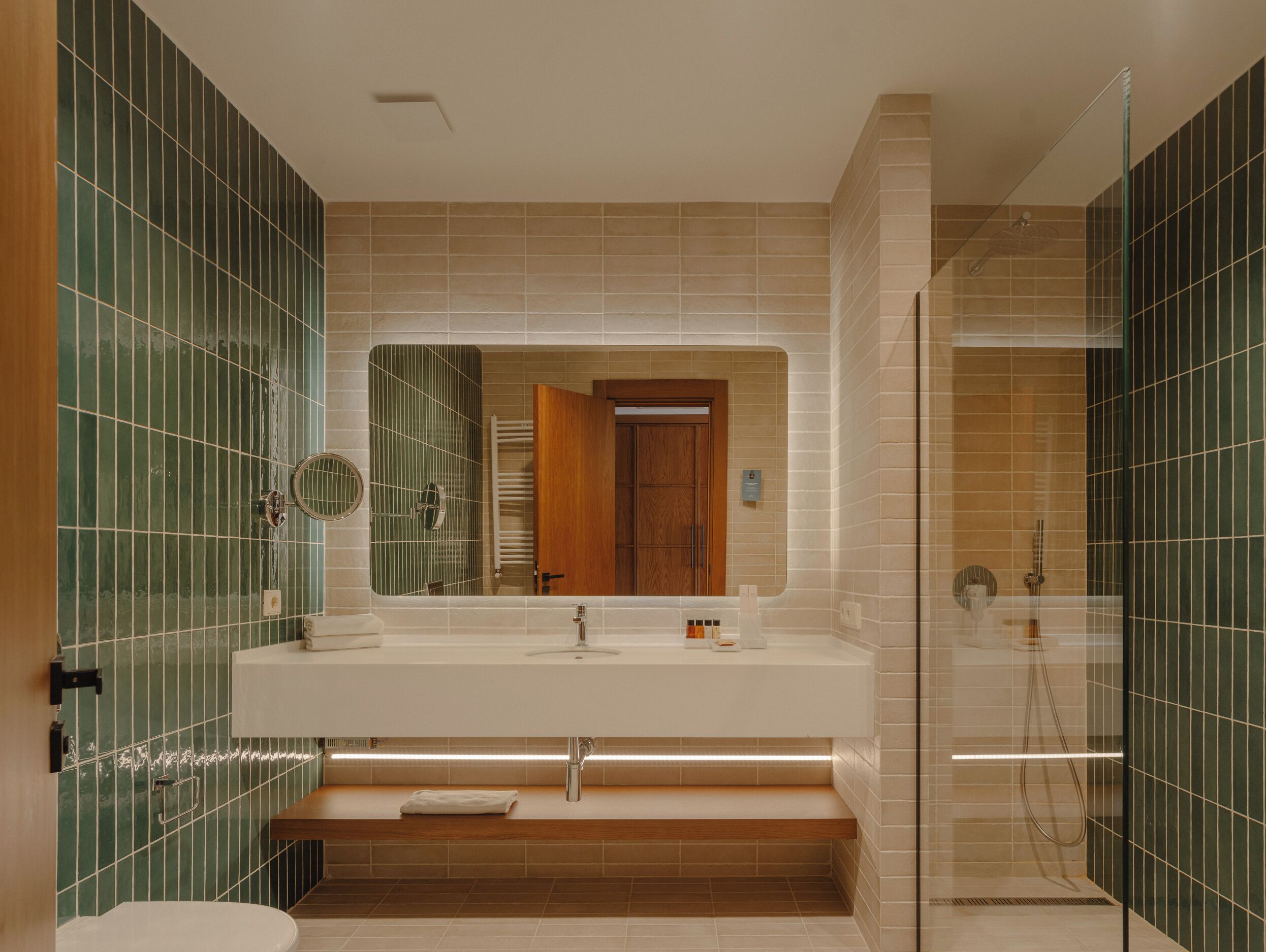 A bathroom with a large mirror, a sink, a toilet, and a shower area.