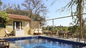 A pool area with lounge chairs and a small building with a tiled roof. - Asiatic Lion Lodge (Mendarda)