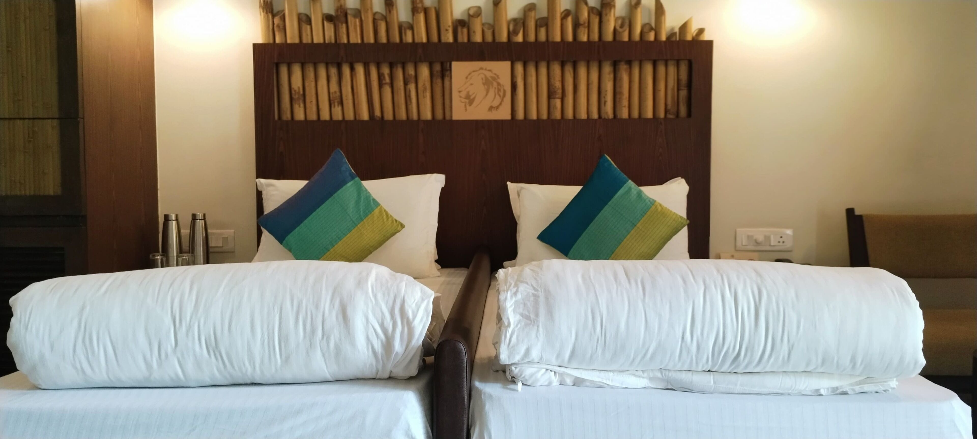 A hotel room with two beds, each with white bedding and decorative pillows. There is a wooden headboard with a bamboo design and a framed picture.
