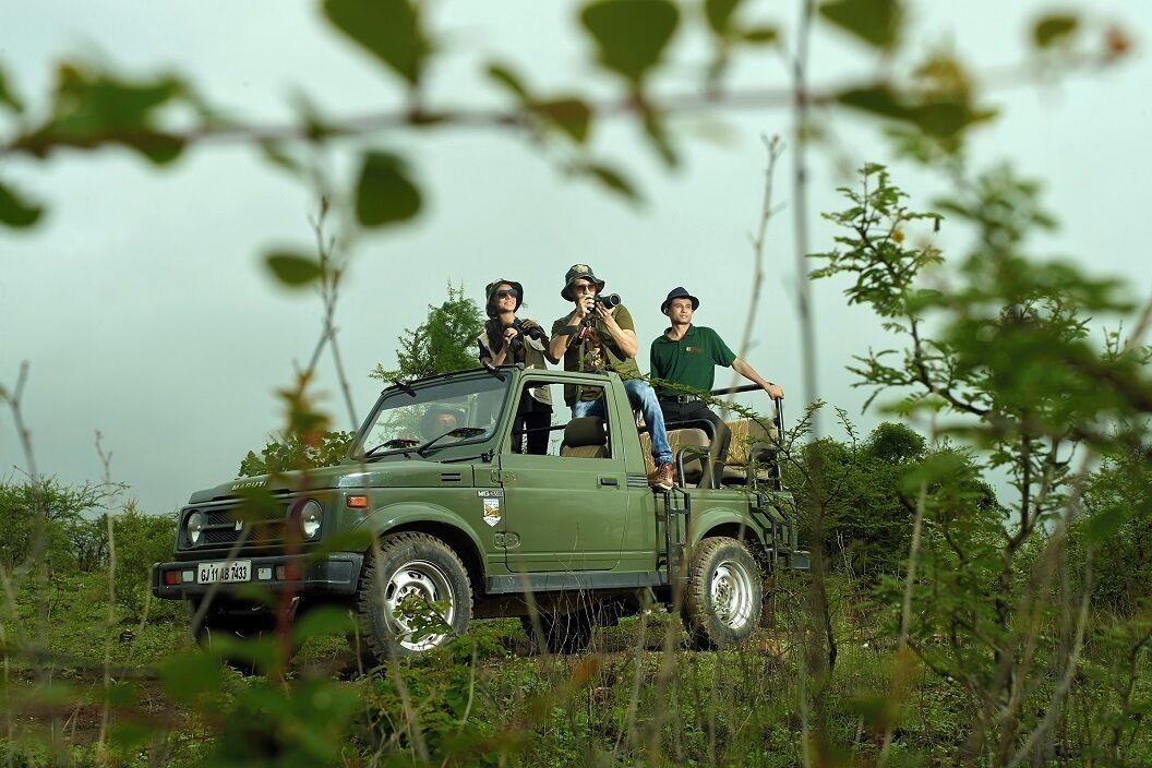 Un vehículo todoterreno verde con tres personas vestidas con equipo de estilo militar, conduciendo por un paisaje natural.