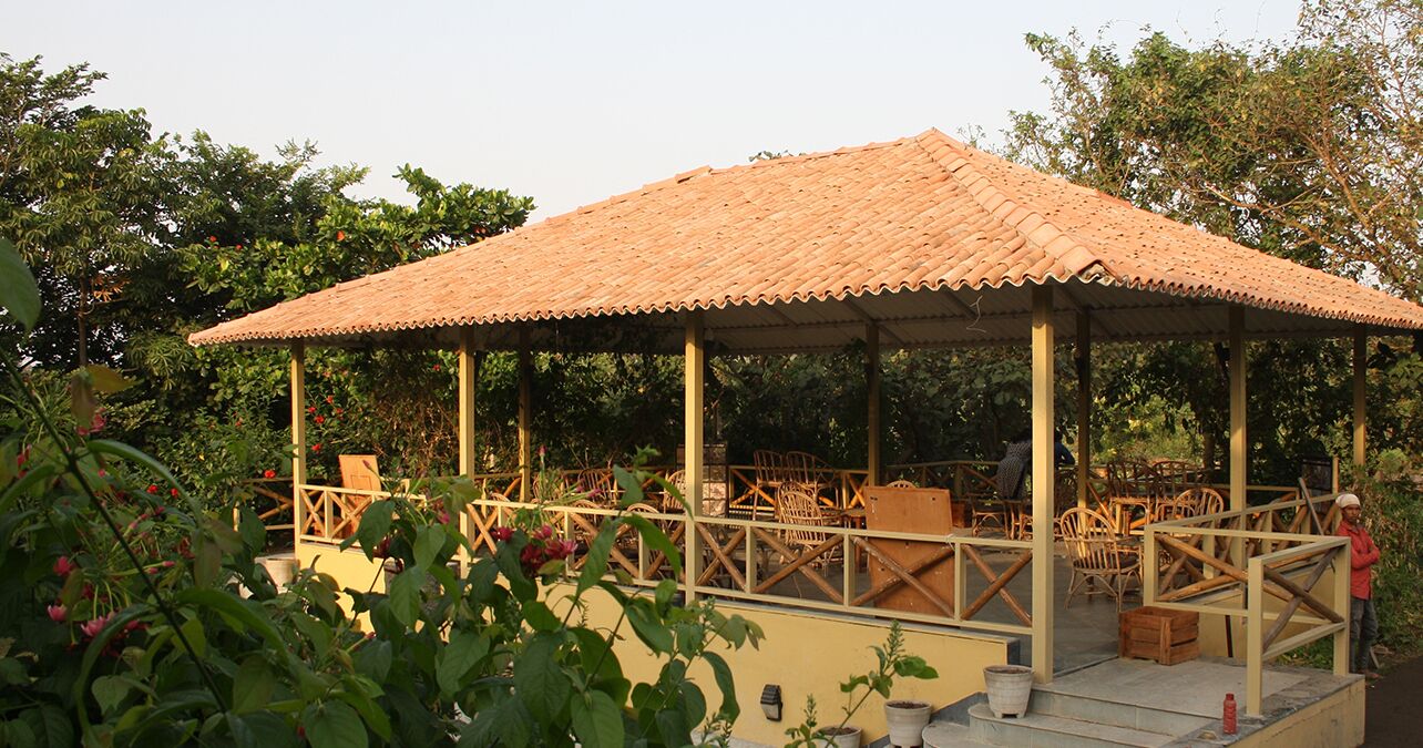 Un área de estar al aire libre con techo, con sillas y mesas de madera, rodeada de abundante vegetación.