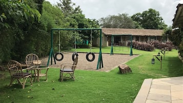Relax in a serene outdoor space with a lawn, rustic guesthouse, and a swing set surrounded by comfortable seating.