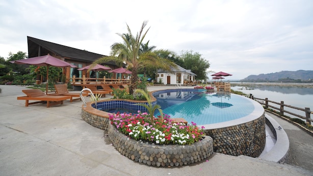A pool area with lounge chairs, umbrellas, and a stone border with flowers. - Myitkyina Plam Spring Resort Hotel (Myitkyina)
