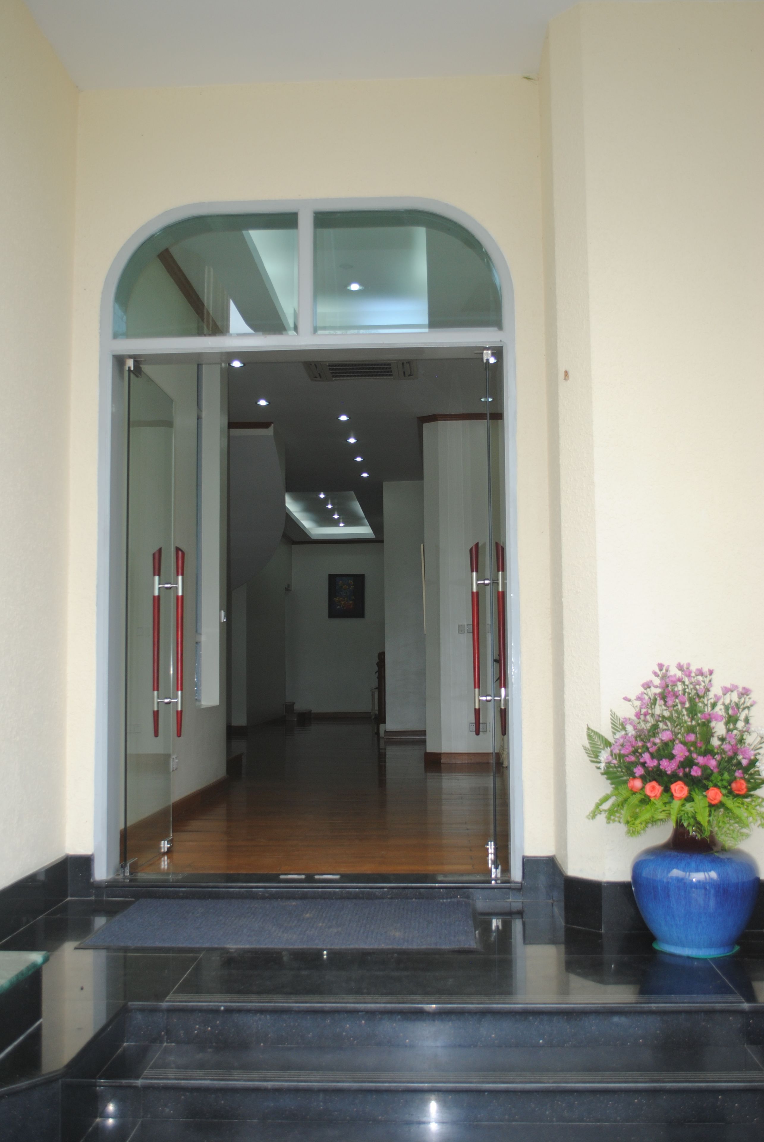 Entrada de hotel con puerta de cristal, una maceta azul y una escalera que conduce al interior.