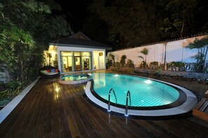 A swimming pool with a wooden deck, surrounded by tropical plants and a house with glass doors. - Myitkyina Plam Spring Resort Hotel (Myitkyina)
