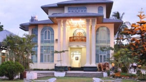 A large, modern building with a central entrance, surrounded by well-maintained gardens and trees. - Myitkyina Plam Spring Resort Hotel (Myitkyina)