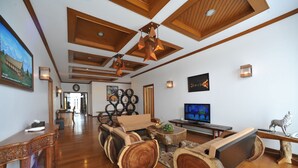 A spacious living room with a wooden floor, a large TV, and a fireplace. There are wooden tables and chairs, and a large painting on the wall. - Myitkyina Plam Spring Resort Hotel (Myitkyina)