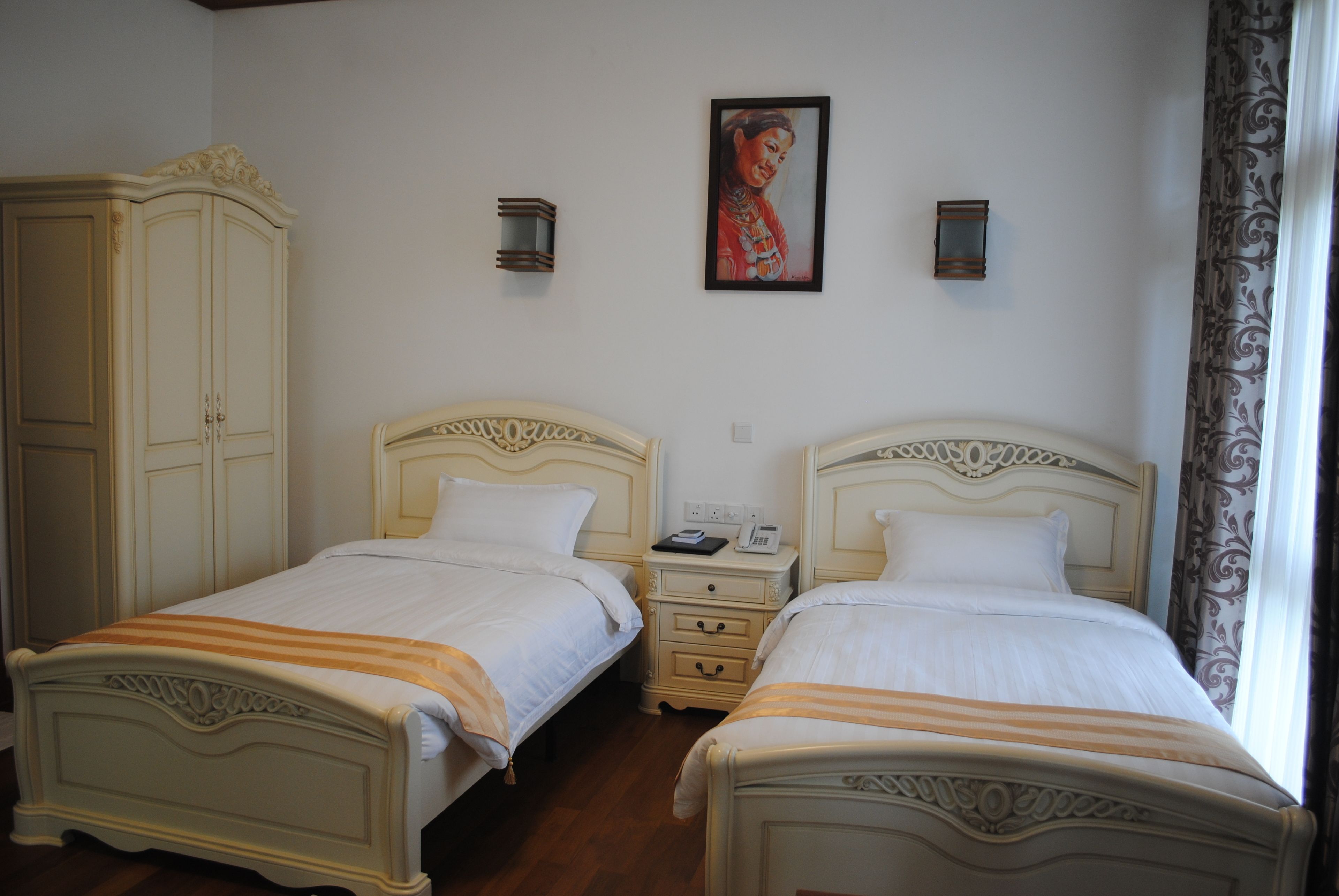 A room with two beds, a wardrobe, a nightstand, and a painting on the wall.
