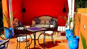 Une pièce aux murs d’un rouge vif, avec un lit, une table et des chaises. On y trouve des plantes en pot et un luminaire suspendu.
