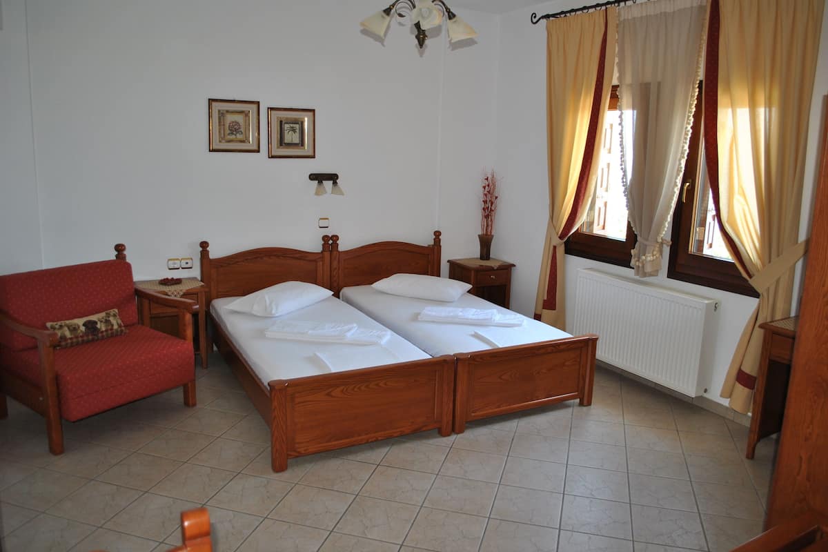 A bedroom with a wooden bed, a red armchair, a bedside table, and a window with curtains.