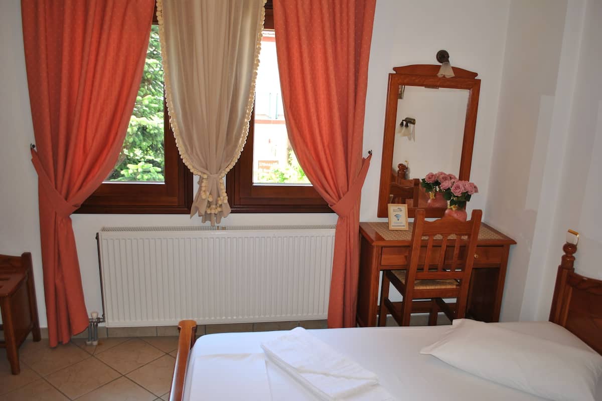 A bedroom with a bed, a wooden dresser, a mirror, and a window with curtains.
