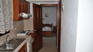 A narrow hallway with a kitchen area on one side, a bed in the other, and a door leading to another room. - Guesthouse Papagiannopoulou (Zagora-Mouresi)
