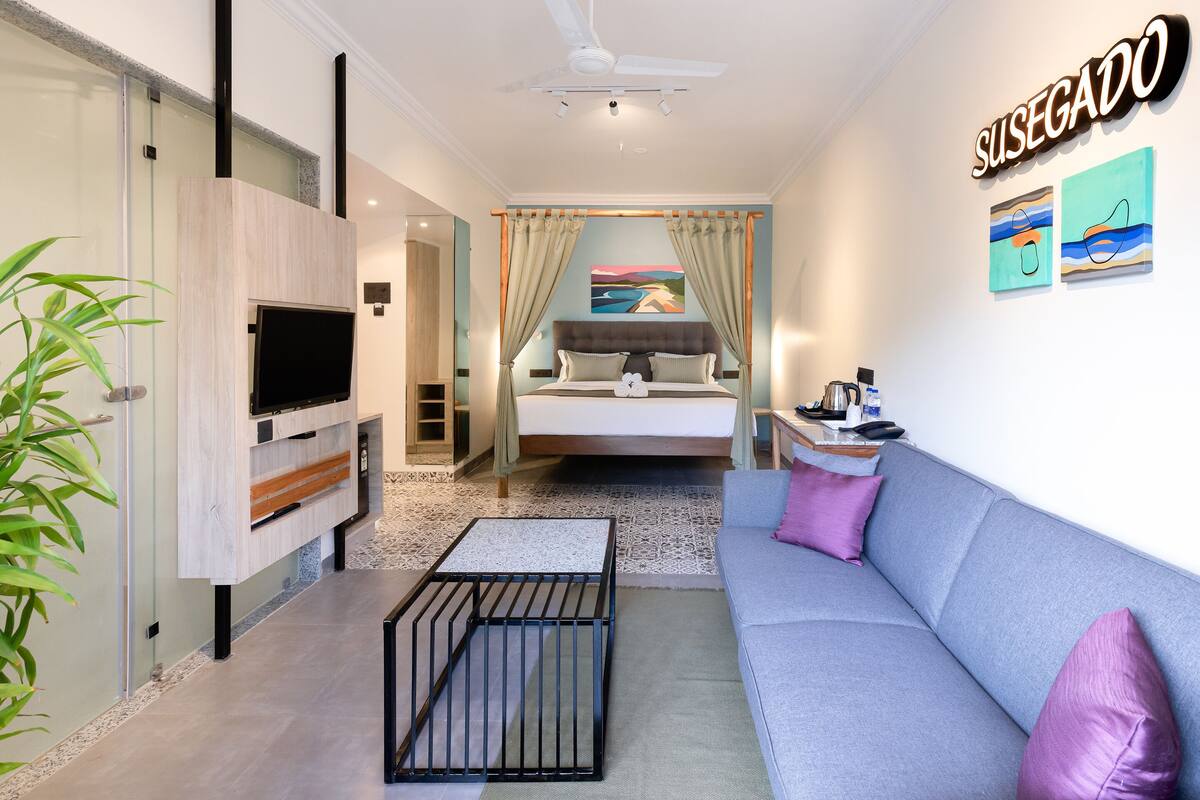 A modern hotel room with a bed, a sofa, a TV, and a desk.
